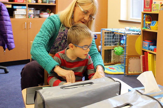 Teacher helping young boy learn to use braille machine image.