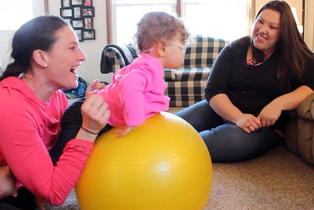 young toddler and physical therapist working otgether as mom looks on image.