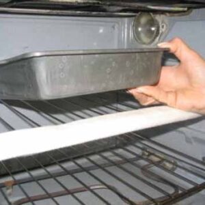 oven rack guard on the front of an oven shelf. A hand reaches into the oven, holding a pan.