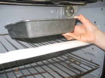 oven rack guard on the front of an oven shelf. A hand reaches into the oven, holding a pan.