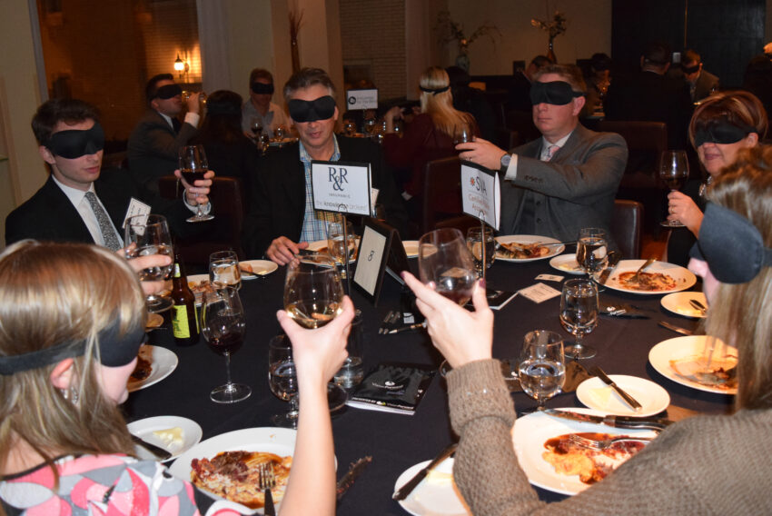 Diners with blindfolds on at dinner make a toast.