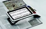 The Smartlux sits on a magazine, the print showing magnified on its screen.
