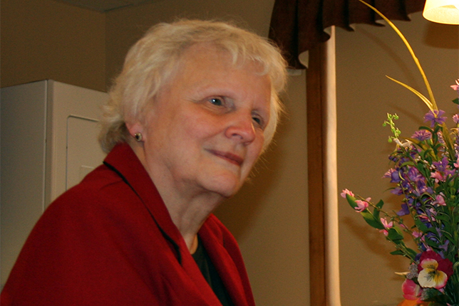 Vision Forward Board Member and volunteer Nona Graves in a red jacket, with a bouquet of spring flowers nearby.