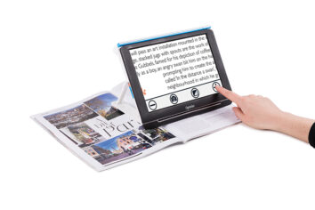 The Compact 10 sits on top of a magazine. A woman's hand is seen reching out to touch the screen.