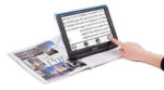 The Compact 10 sits on top of a magazine. A woman's hand is seen reching out to touch the screen.