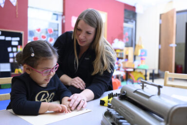 Photo of Colleen Kickbush working with a child on a brailler.