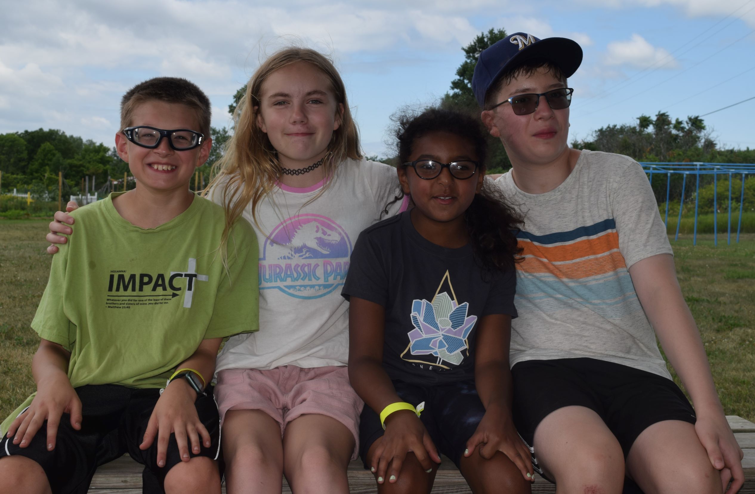 Group of four youth sitting on a bench at camp.