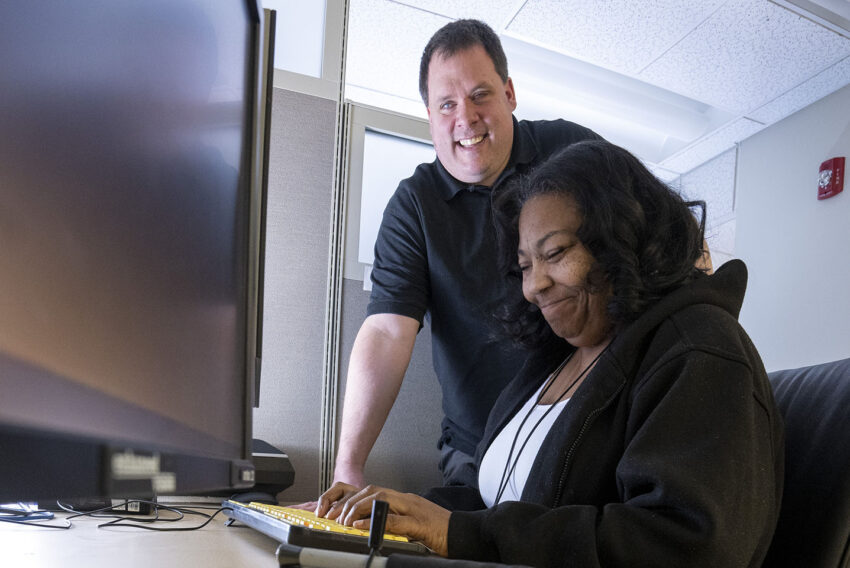 Smiling woman typing on computer keyboard with guidance from trainer.