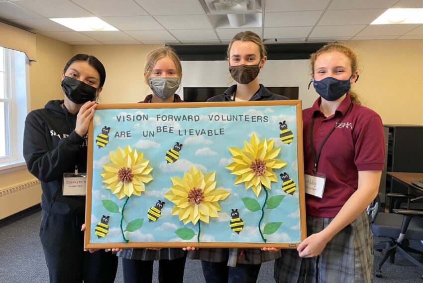 volunteer kids holding a sign that says Volunteers are Unbelievable with bumblebees