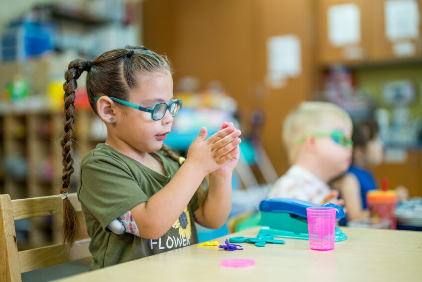 little girl with glasses at table playing with toys