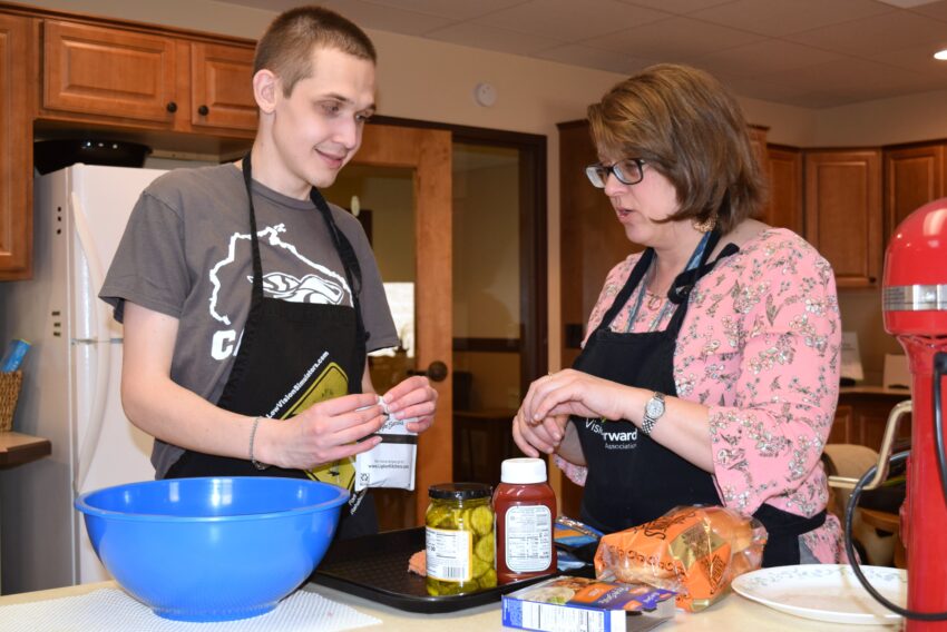 Young man with visual impairment puts ingredients into bowl to cook with help of occupational therapist