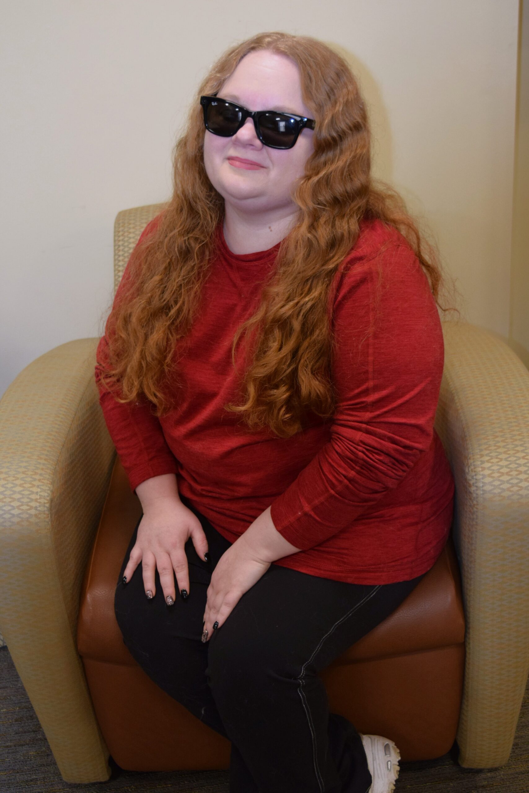 woman with long wavy red hair, black glasses and a red long sleeved shirt