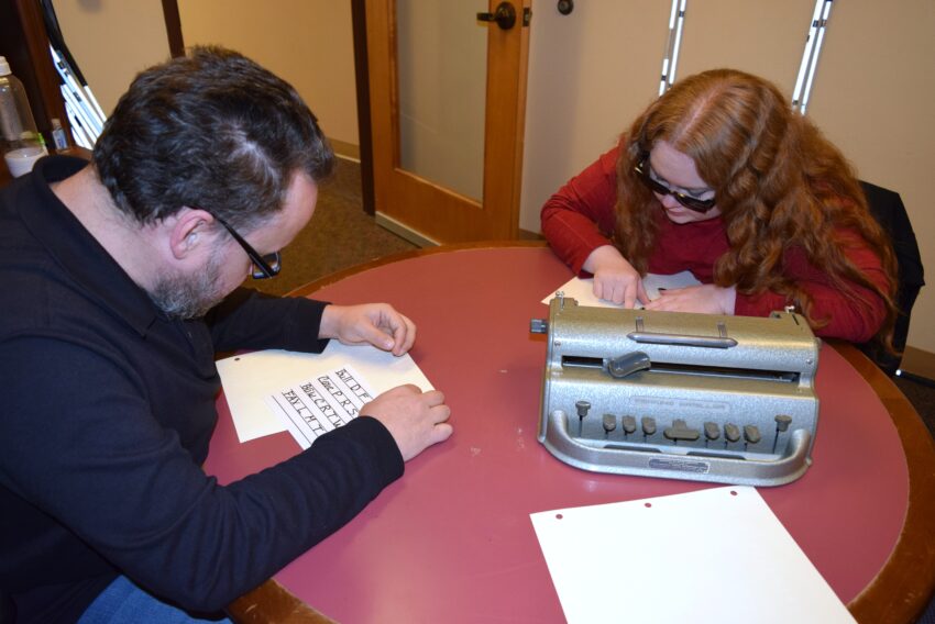 woman reading braille with teacher at a table