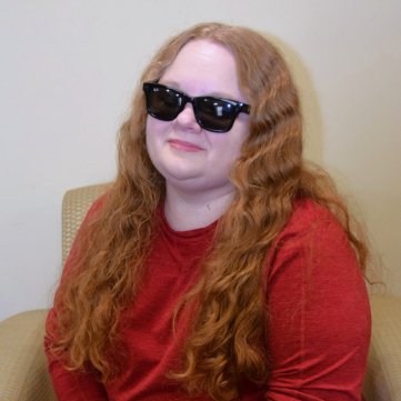 woman with long wavy red hair, black glasses and a red long