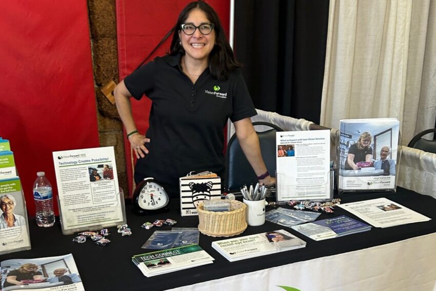 woman standing behind a table with lots of brochures and the words vision forward on the table cloth in front