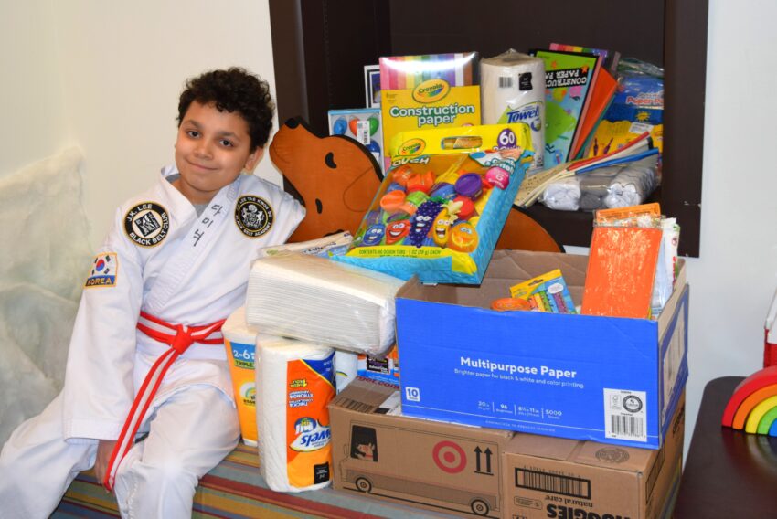 dark haired boy with a tae kwan do uniform sitting next to a pile of donations