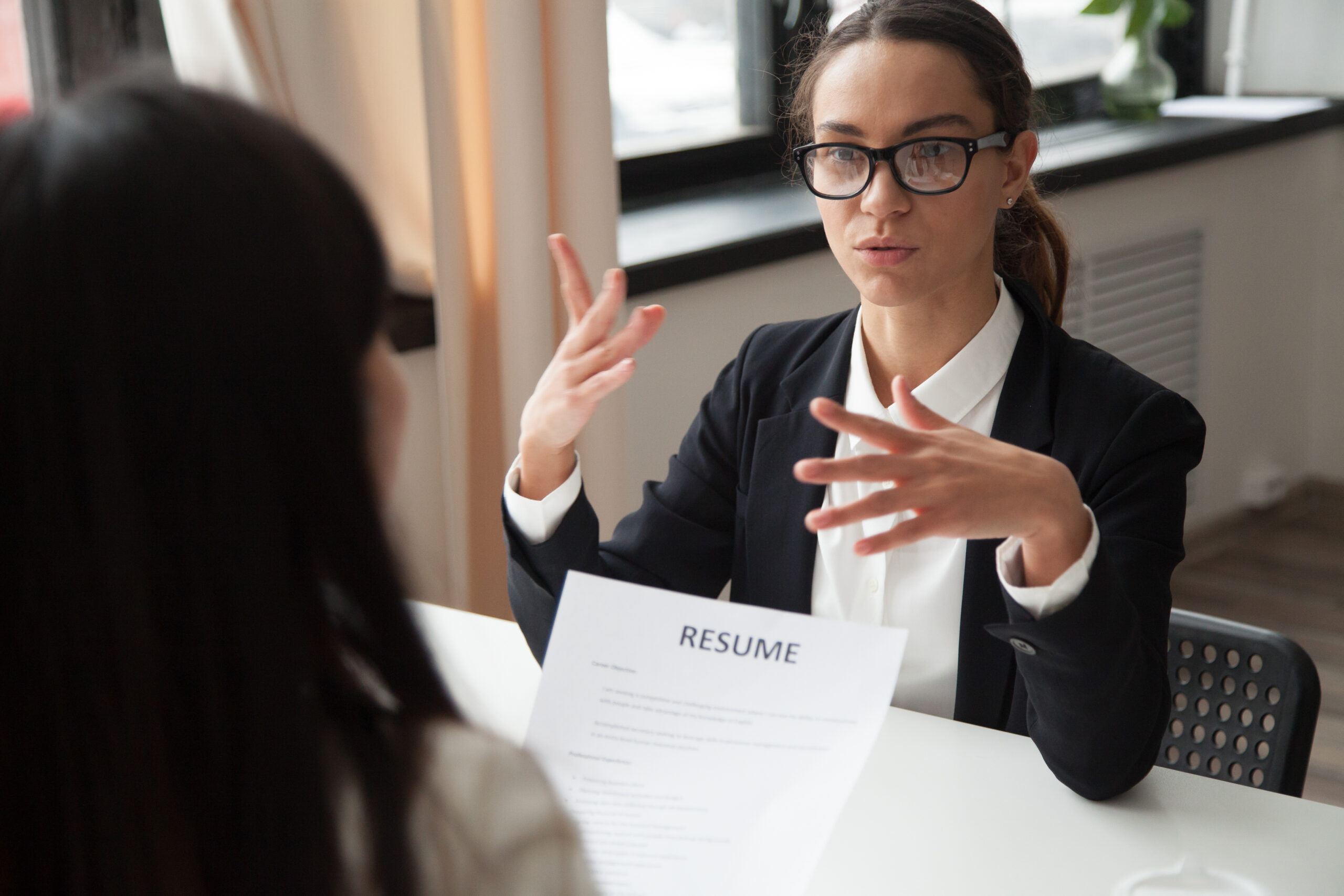 woman with glasses gesturing in interview with someone across the table with her resume