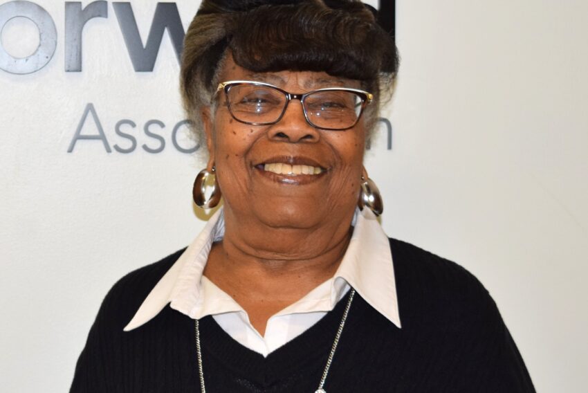 Older black woman dressed in black sweater and white blouse with glasses and hoop earrings on.
