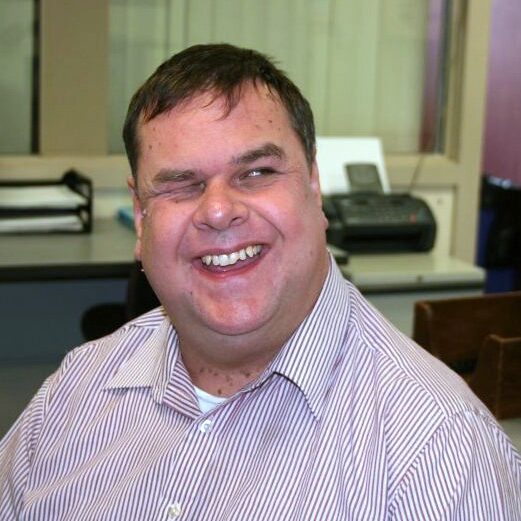 older man with big smile dark hair and a striped shirt on