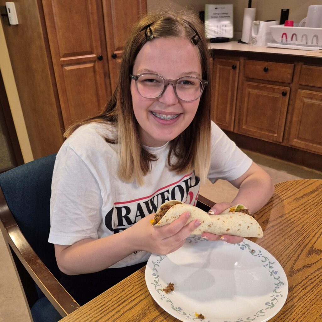 Girl with long hair ad glasses holding a taco over a plate