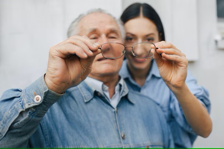 an older man and younger woman behind him looking through a pair of glasses