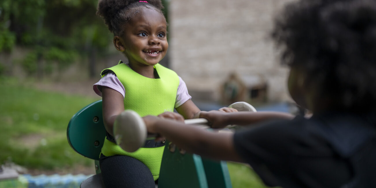little girl of color playing on a playground toy with a big smile