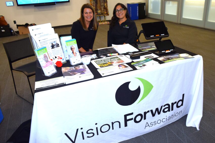 two women smiling and sitting at table with printed brochures for vision forward