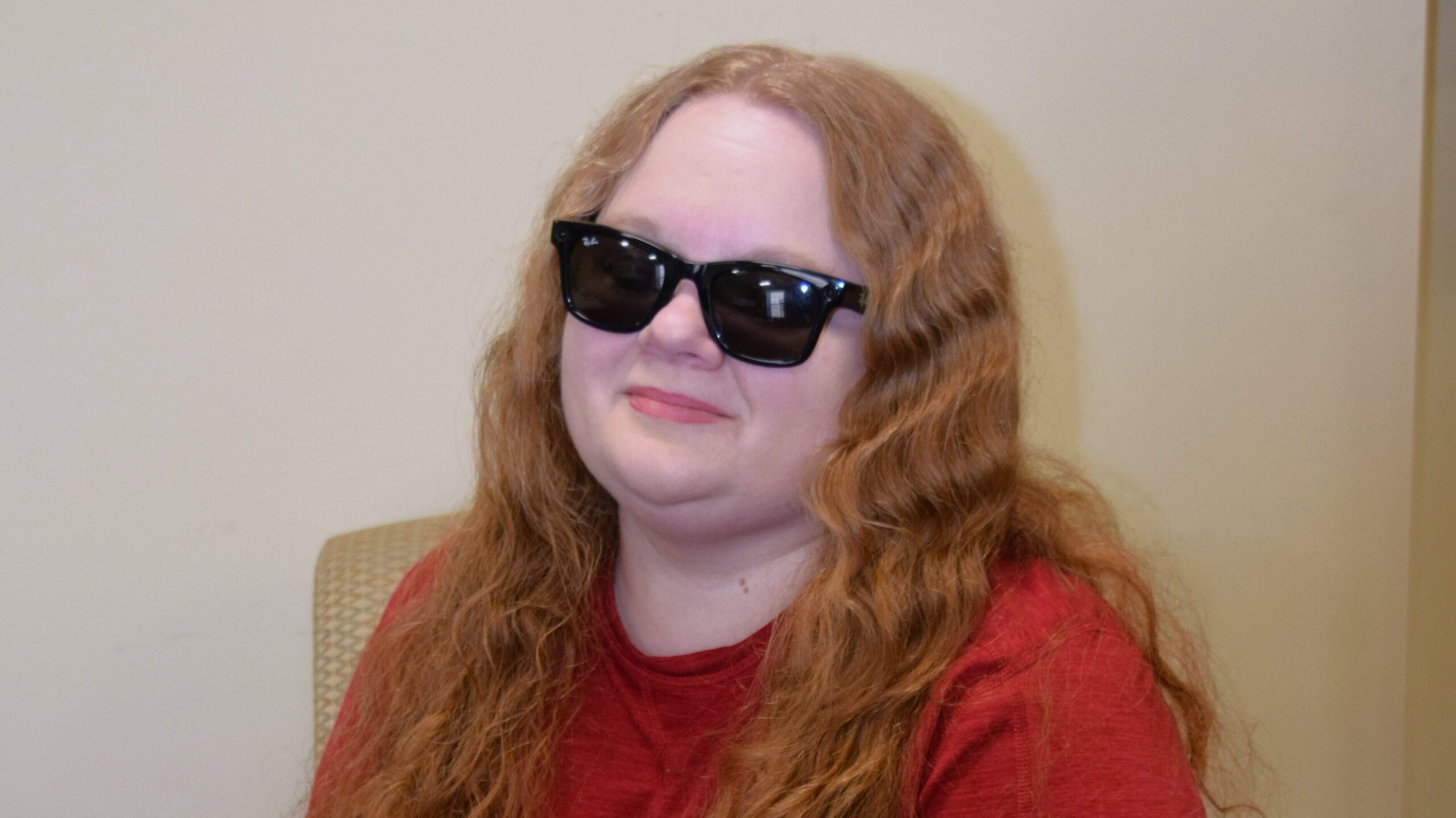 woman with long wavy red hair, black glasses and a red long sleeved shirt