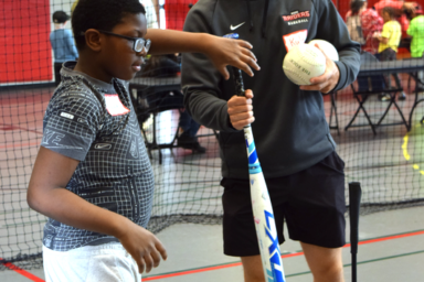 young man helping a boy locate the ball with a bat in his hand