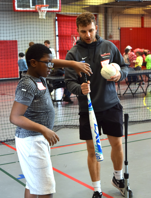 young man helping a boy locate the ball with a bat in his hand
