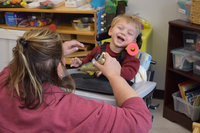 little boy in high chair smiling and working with a therapist