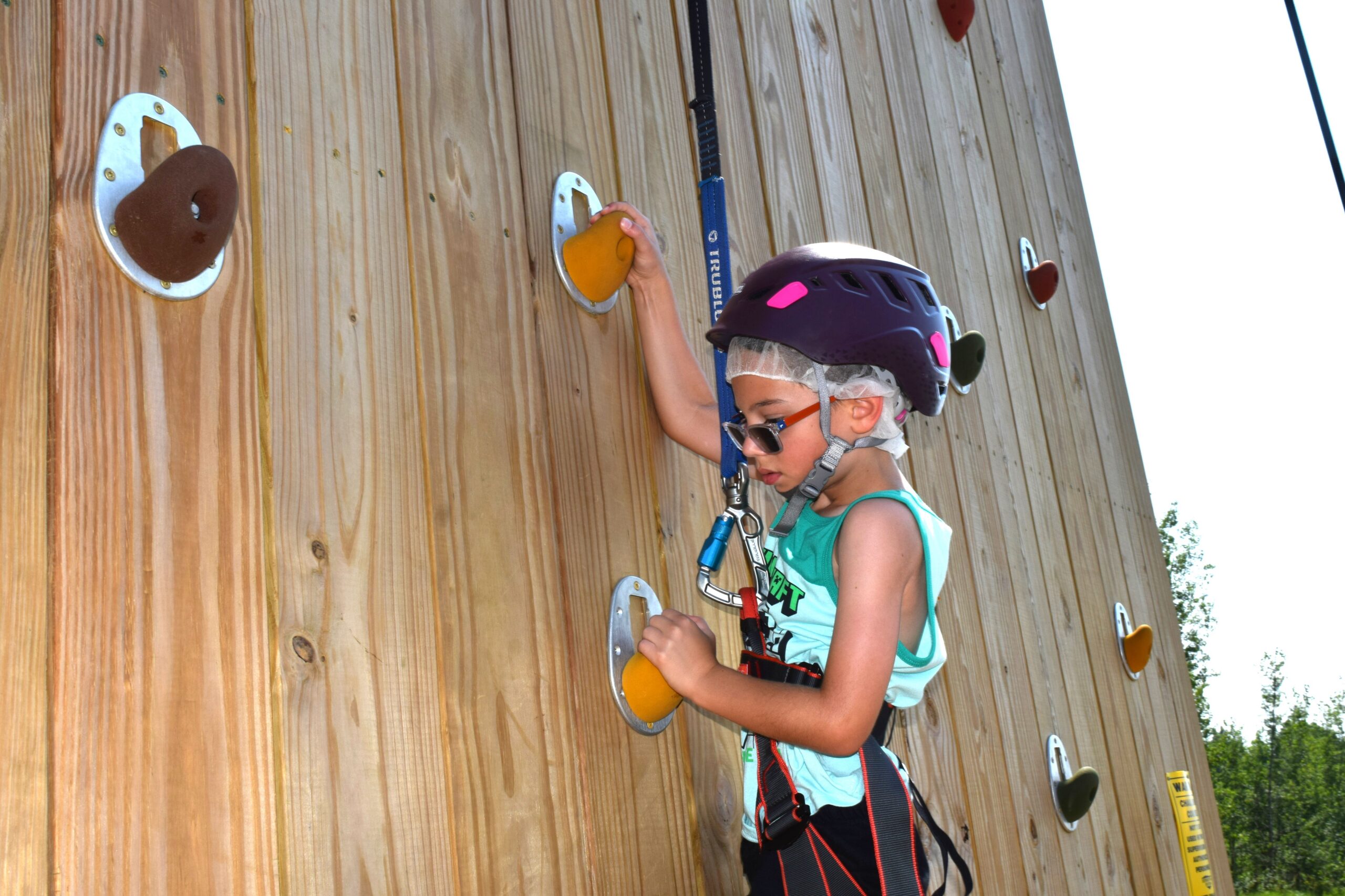 boy climbing up a rock wall with a harness and safety helmet on