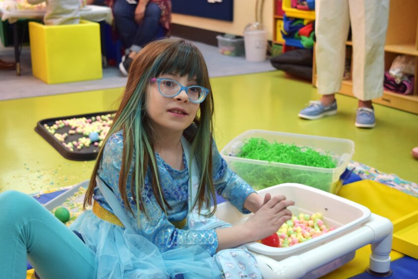 young girl with glasses on playing in a bucket filled with sensory items