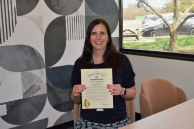 Vision Forward CEO Jacci is holding the certificate while seated and smiling