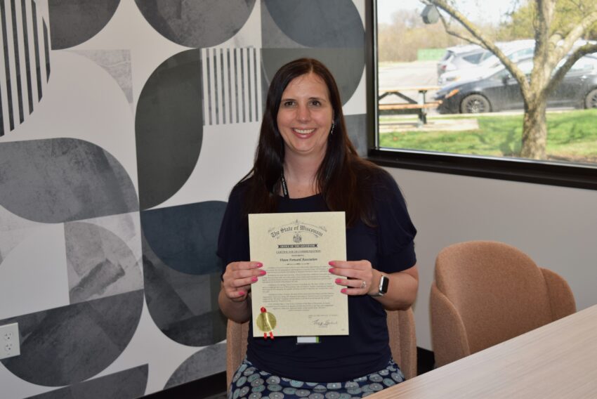 Vision Forward CEO Jacci is holding the certificate while seated and smiling