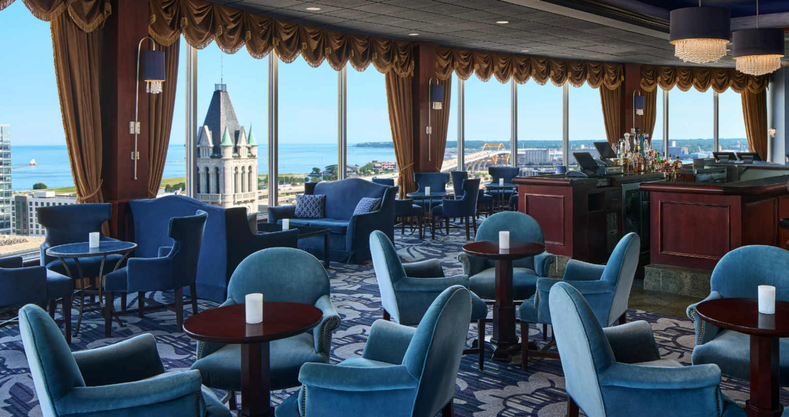 Elegant room filled with blue chairs a huge bay window looking out over the city and a bar