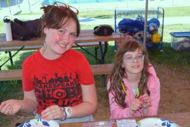 Older girl sitting with a younger girl at a park bench smiling and looking at the camera