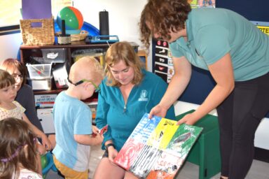 two women showing a little blond boy a book