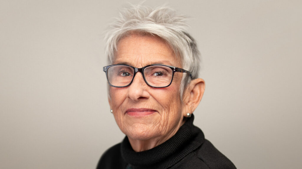 older woman with white short hair and black glasses.