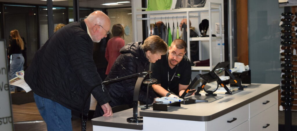 A young man shows an older couple an electronic magnification device in the Vision Forward Store.